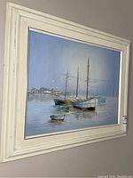 Front view of framed sailboat harbor painting with white wooden frame and matting.