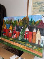 Painting showing full row of colorful houses, lamppost, trees and sky, leaning on a box.