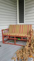 Wide shot of painted bamboo loveseat with striped cushions on a porch, showing condition and structure.