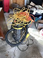 Full view of Stanley wet/dry vacuum on wheels with coiled extension cords on top, showing vacuum hose and power cord.