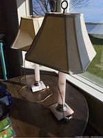 Pair of matching lamps on a wooden surface near window with view outside, showing square tapered shades and blush marble-like resin bases