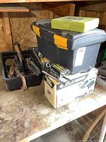 Photo of stacked toolboxes and other items on workspace bench showing two plastic toolboxes, a Radley hole saw kit, and other boxed tools.
