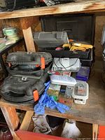 Shows two Black & Decker Mouse sanders in their plastic cases, Weller soldering tool, clamps, connectors, steel wool, cordless Benchmark tool, gloves, and a toolbox on a rustic workbench.