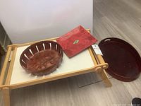 The folded wooden bed and breakfast tray with a white surface, red glass square tray, and the round wooden basket tray seen on the tray base.