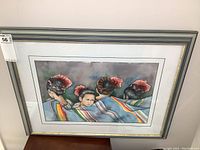 Framed watercolor painting displaying four girls wrapped in colorful blankets, photographed from the front showing entire artwork and frame.
