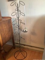 Full view of metal wine bottle tree with circular holders for wine bottles and hooks for small cups.