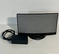 Bose SoundDock speaker system with grey fabric front and black body accompanied by a power adapter with cable.