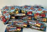 Photo showing 17 boxed motorized toy trains from Mighty Express series arranged on a flat surface, displaying various engine versions, packaging in clear plastic and blue backing.