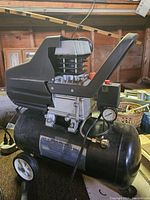 Side view of the black air compressor with metal cooling fins and pressure gauge visible.