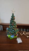 Front view of a green glazed ceramic Christmas tree with colorful bulbs and translucent star top. Power cord visible.