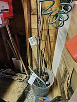 Fishing poles standing in a gray plastic tub, with attached reels visible. A green-handled fishing net with metal frame is leaning on the tub.