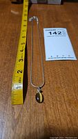Full view of necklace with metal chain and Tiger Eye pendant next to measuring tape showing length