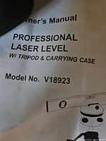 Close-up photo of user manual showing professional laser level title, model number V18923, and mention of tripod and carrying case