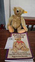Front view of the golden beige Steiff teddy bear sitting next to the Teddy Bear Catalog book illustrating the lot contents.
