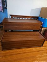 Two wooden trundle chests placed one over another against a wall, showing solid wood finish and rectangular shape.