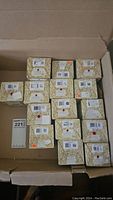 Top-down view of approx 15 boxed porcelain figurines showing barcodes and packing inside a cardboard box.