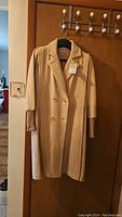 Front view of vintage beige wool coat with double-breasted gold buttons and ribbed cuffs.