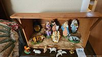 Overall view of the wooden manger with all nativity figures arranged inside on straw base.