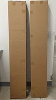 Two tall sealed cardboard boxes leaning against wall
