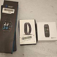 Three boxed smartwatches side by side: GRDE, fitness tracker, Koretrak