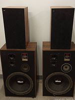 Front view showing two large and two smaller Beovox speakers with wood veneer and black grills.