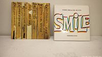 Two items: one a vintage handwritten set of Beach Boys 45 RPM tape boxes, and the other a Beach Boys book titled 'SMILE Sessions'.