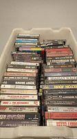 Top view of a bin full of cassette tapes stacked tightly, showing labels of various artists such as James Taylor, Mike + The Mechanics, Belinda Metz, and others.