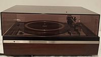 Dual 1228 turntable with dust cover closed, showing wooden base and tinted cover.