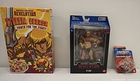Image showing all three items: unopened Eternia Crunch cereal box, Revelation He-Man figure in window box, and mini Battle Armor He-Man small sealed figure.