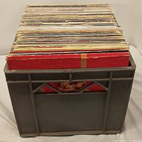 Grey plastic crate filled with numerous vinyl records seen from side
