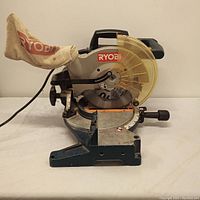 Side view of the Ryobi compound miter saw showing blade guard, dust bag, and base.