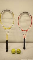 Two tennis rackets and two tennis balls laid side by side vertically against a plain background.