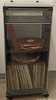 Stereo stand containing vinyl records arranged on three shelves inside protective transparent doors, front view.