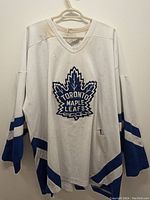 White Toronto Maple Leafs hockey jersey with visible tear near front bottom and stains, blue stripes on sleeves and bottom hem.