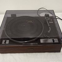 Full front view of Pioneer PL-10 turntable with clear dust cover in place showing wood grain base and control switches.