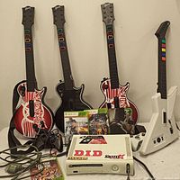 Four guitar controllers, console, controllers and games on table