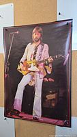 Full view of the poster depicting Eric Clapton playing guitar on stage, mounted with pushpins on a corkboard surface.