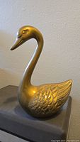 Side view of brass swan figurine showing its profile, engraved feathers, and smooth, curved neck.