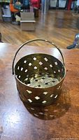 Small brass woven basket on a wooden surface, showing the full basket with handle in upright position.