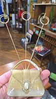 Front view of gold purse-shaped photo clip holder showing faux pearl decoration and three wire photo clips