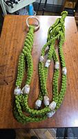 Photo showing full length view of green macrame plant hanger with clear beads placed along the cords and a clear ring for hanging.