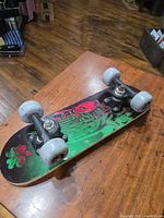 Mini skateboard on wooden surface showing entire deck and wheels, highlighting graphic design and condition.