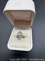 Ring in white jewelry box with cream interior showing front angled view of marquise aquamarine in filigree mount