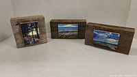 Three wood mounted prints arranged side by side showing distinct landscape scenes mounted on wood blocks.
