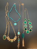 Six necklaces displayed on black background, showing blue and green stones with gold-tone chains.