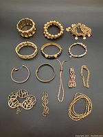 All 14 gold coloured bracelets arranged flat on a dark surface showing different styles and sizes in one image.