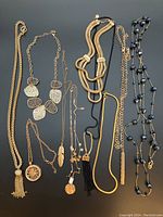 Lot of black and gold colored costume necklaces arranged side by side showing different chain and pendant styles.