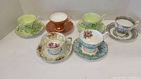 Overall view of six different cups and saucers from Royal Albert, Aynsley, and DelMar arranged on a white surface
