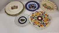 Seven pieces: a Royal Doulton Bunnykins bowl and six decorative plates with varied designs, including commemorative, floral, royal portraits, countryside scenes, and crests.