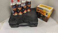 Lot showing black carrying case with Coleman stove, four butane fuel cans, and Yanes stove box arranged on a white surface.